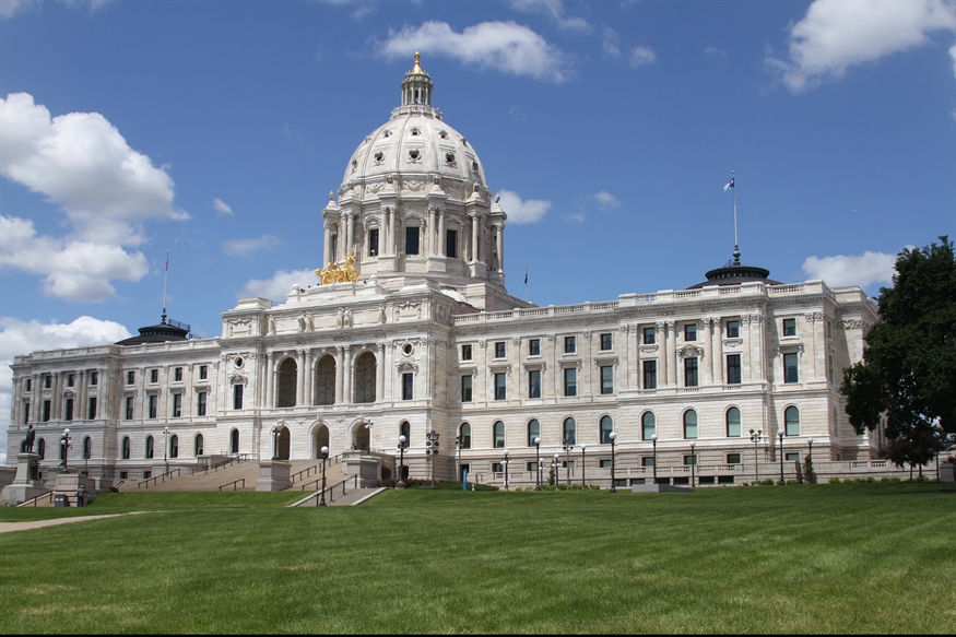 Exterior view of the Minnesota State Capitol building in St. Paul on a sunny day, featuring its white marble facade, grand staircase, central dome with a gold-leaf sculpture, and the new Minnesota state flag flying at the top Exterior view of the Minnesota State Capitol building in St. Paul on a sunny day, featuring its white marble facade, grand staircase, central dome with a gold-leaf sculpture, and the new Minnesota state flag flying at the top